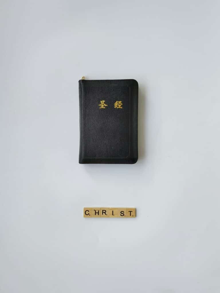 A black leather Chinese Bible with Scrabble tiles spelling 'CHRIST' on a white background.